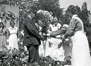 Bloemen bij het monument voor koningin Emma in Amsterdam, 29 juni 1940. De vrolijke verpleegsters komen uit de Valeriuskliniek, om de hoek bij het monument.