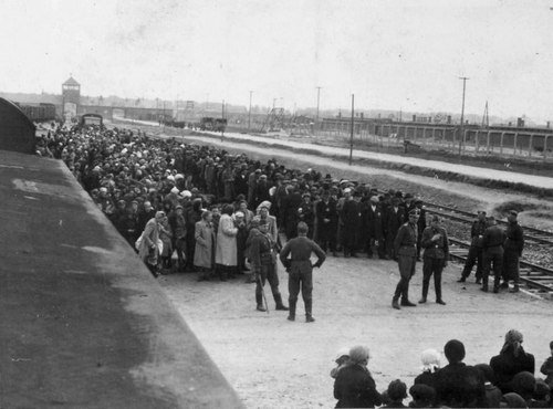 Mannen en vrouwen werden na aankomst op het perron van Auschwitz van elkaar gescheiden. Op de achtergrond de toegangspoort tot het kamp.