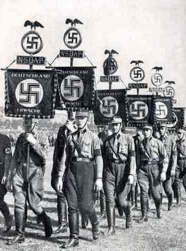 Nazi's dragen vaandels met hakenkruizen bij een partijbijeenkomst.